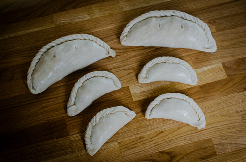 Six uncooked pasties arranged on a wooden surface.
